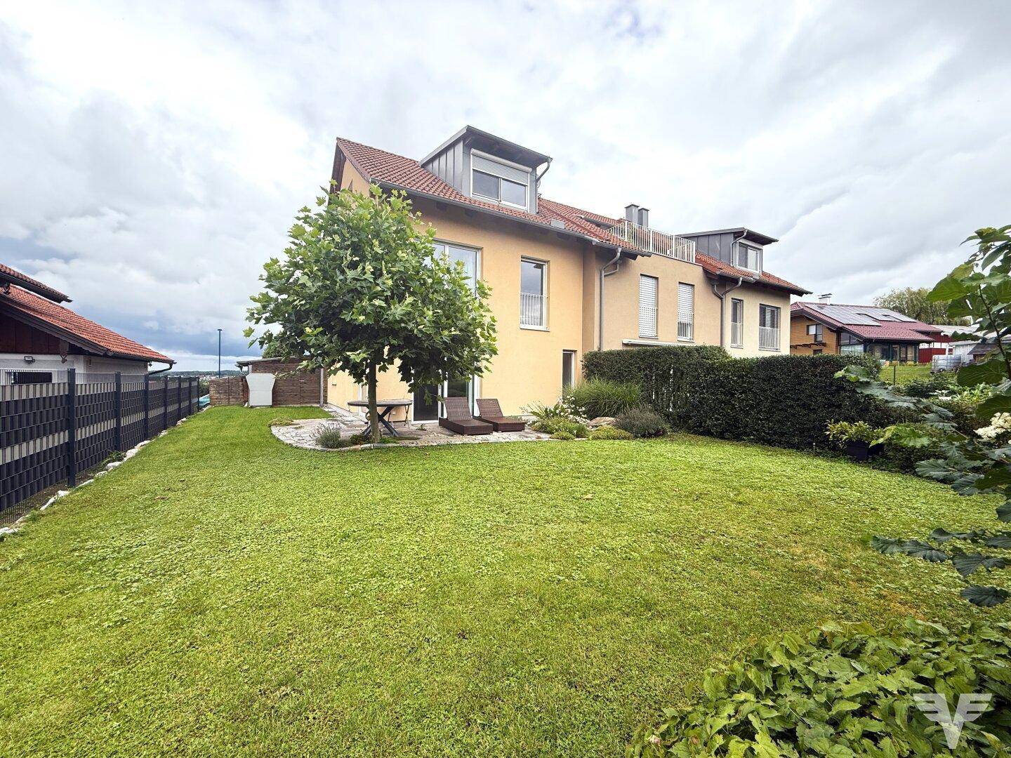 Gepflegter Gartenbereich mit Rasenfläche, Bäumen und einer kleinen Terrasse hinter dem Haus.