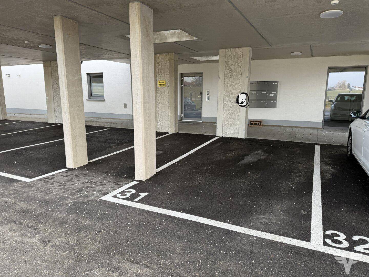 Überdachter Parkplatz mit nummerierten Stellflächen und Ladestation für Elektrofahrzeuge.
