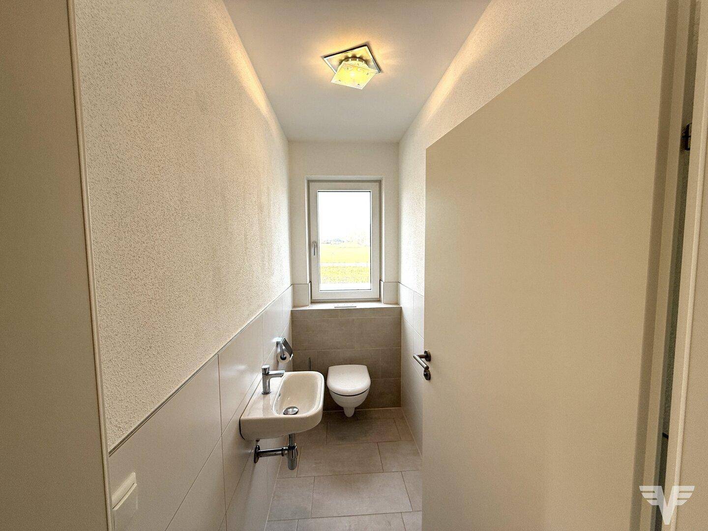 Separates Gäste-WC mit Fenster, wandhängender Toilette und kleinem Waschbecken.