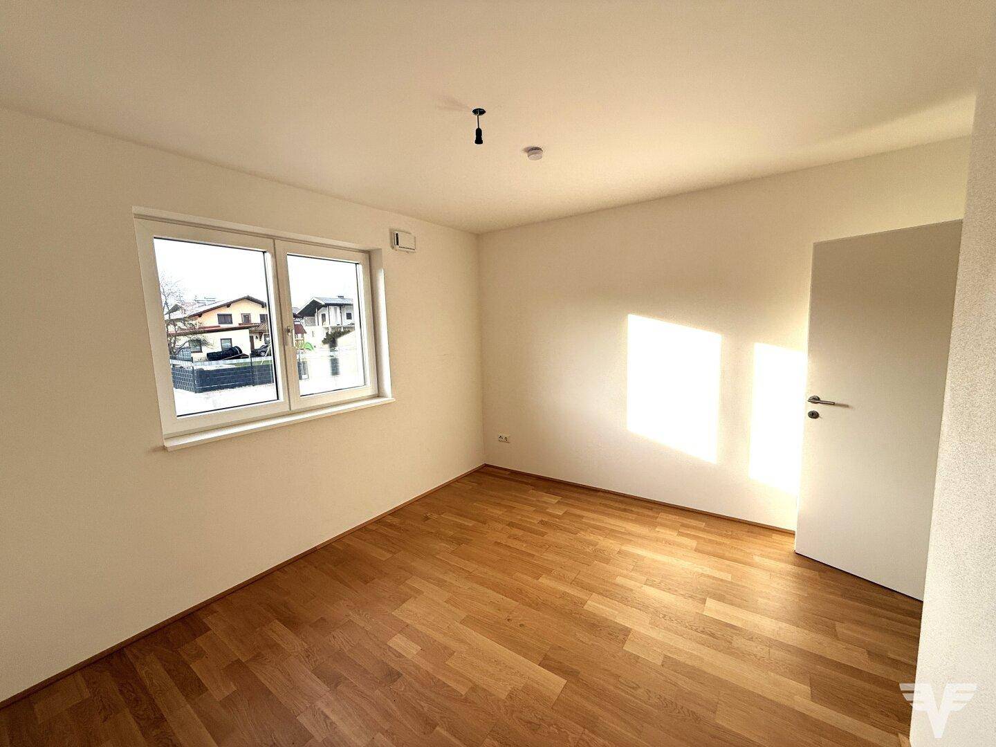 Helles Schlafzimmer mit Holzboden und großem Fenster, das viel Tageslicht hereinlässt.