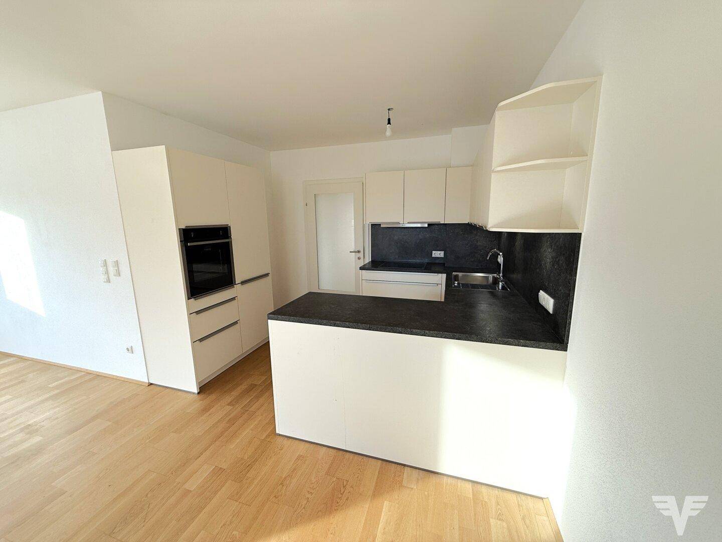 Moderne Einbauküche mit weißen Schränken, dunkler Arbeitsplatte und integriertem Backofen.
