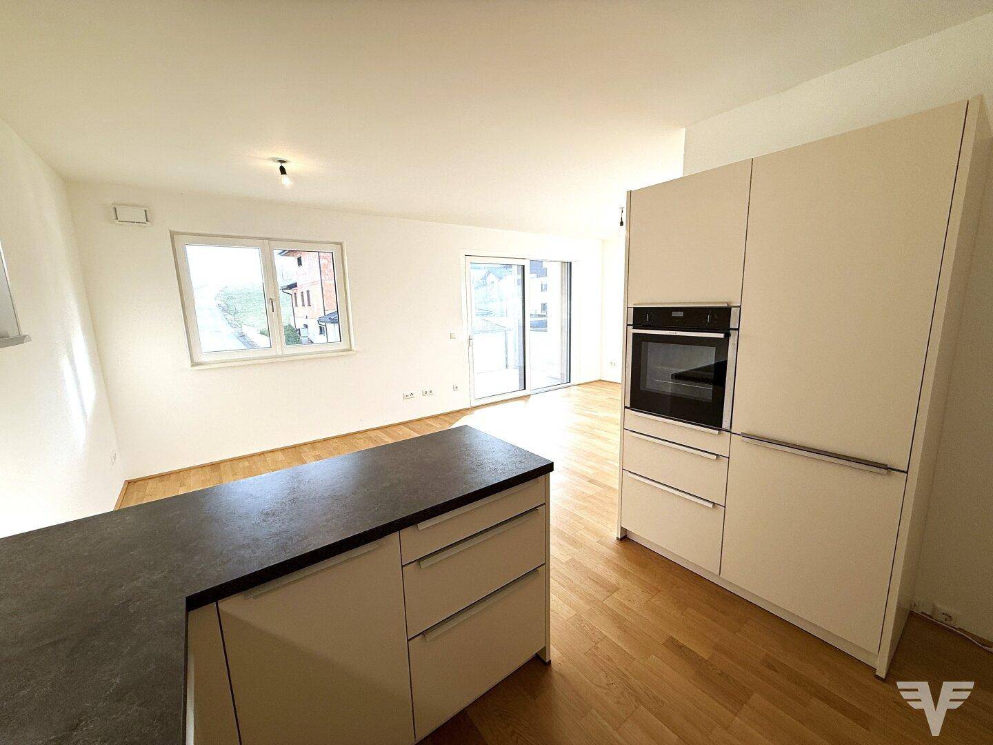 Heller Wohnbereich mit Holzboden und Zugang zu einem Balkon, direkt neben der Küche.