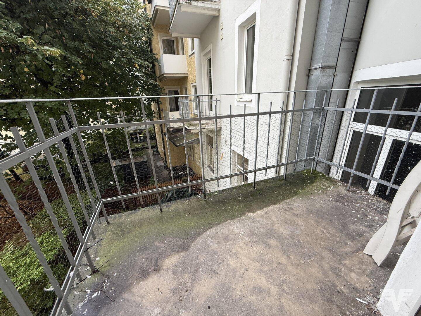 Kleiner Balkon mit Metallgeländer und Blick auf den Innenhof, der Renovierungsbedarf zeigt.