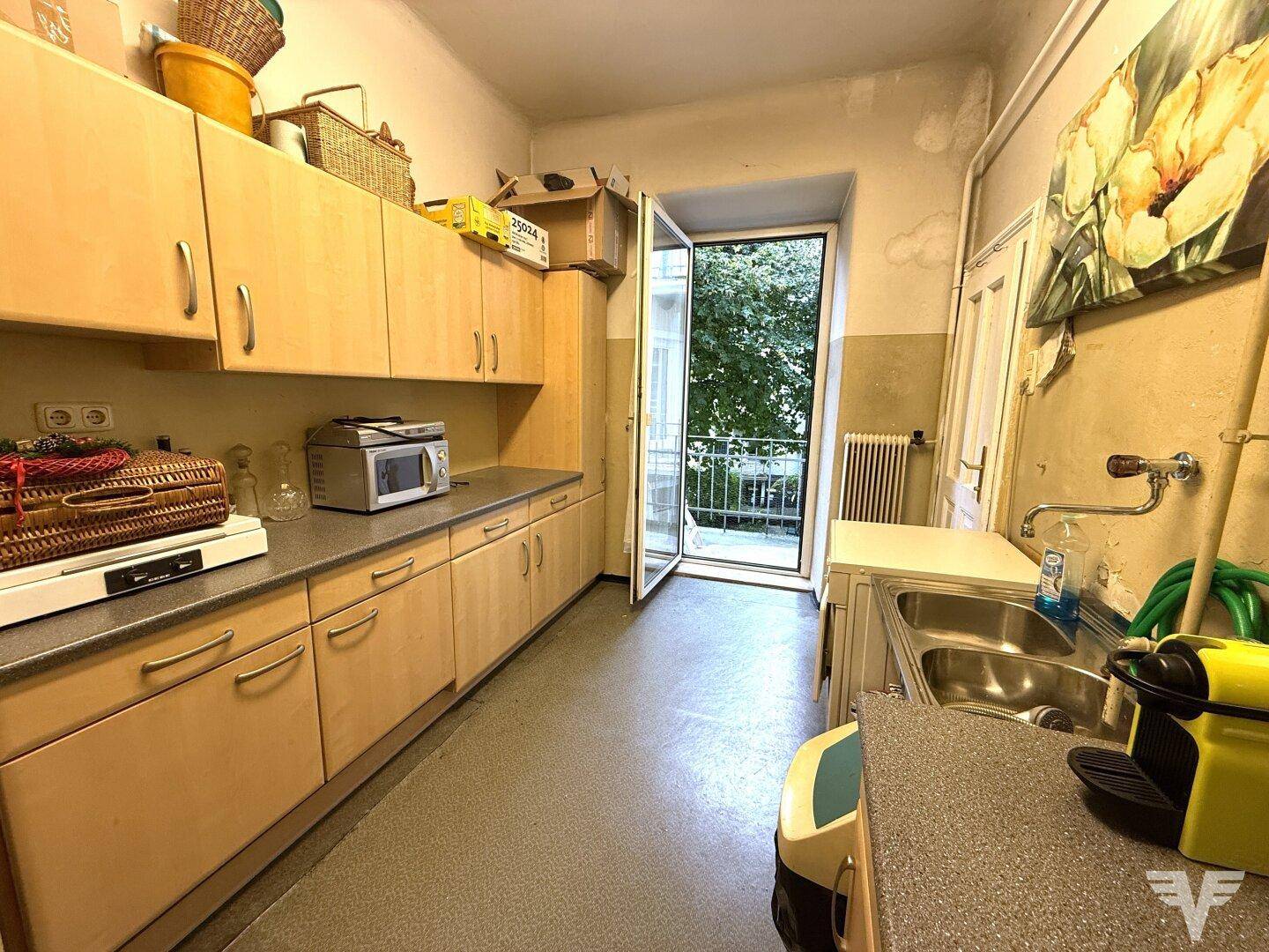 Funktionale Küche mit hellen Holzschränken, Laminatboden und Zugang zu einem kleinen Balkon.