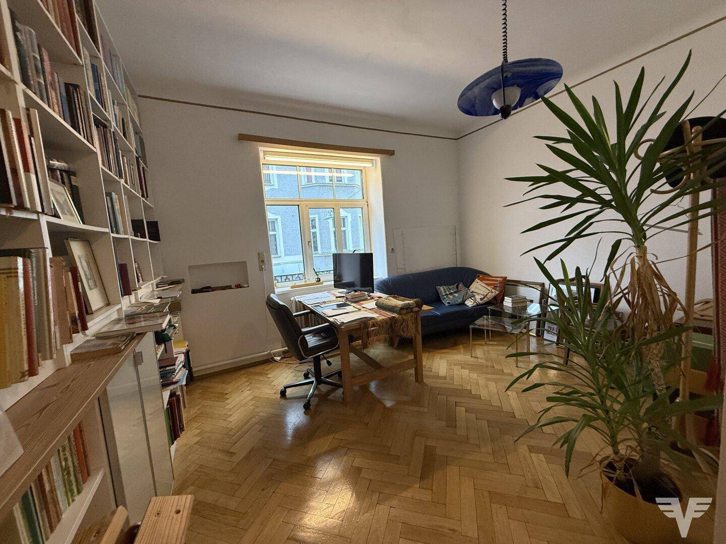 Helles Arbeitszimmer mit umfangreichen Bücherregalen, Parkettboden und Blick auf die städtische Umgebung.