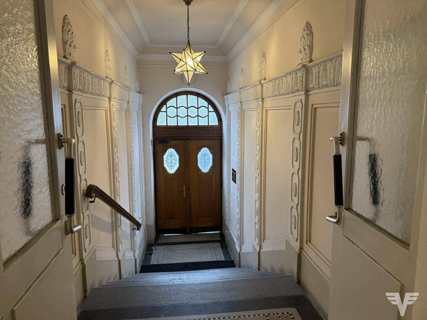 Historischer Eingangsbereich mit Stuckverzierungen, Holztüren und einer dekorativen Sternenlampe.