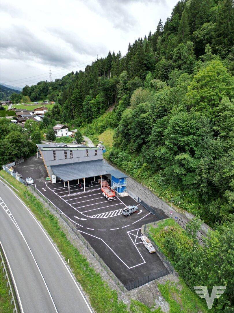 Weitläufige Luftaufnahme des Gewerbeareals mit Parkplätzen, umgeben von Wald und einer Landstraße.