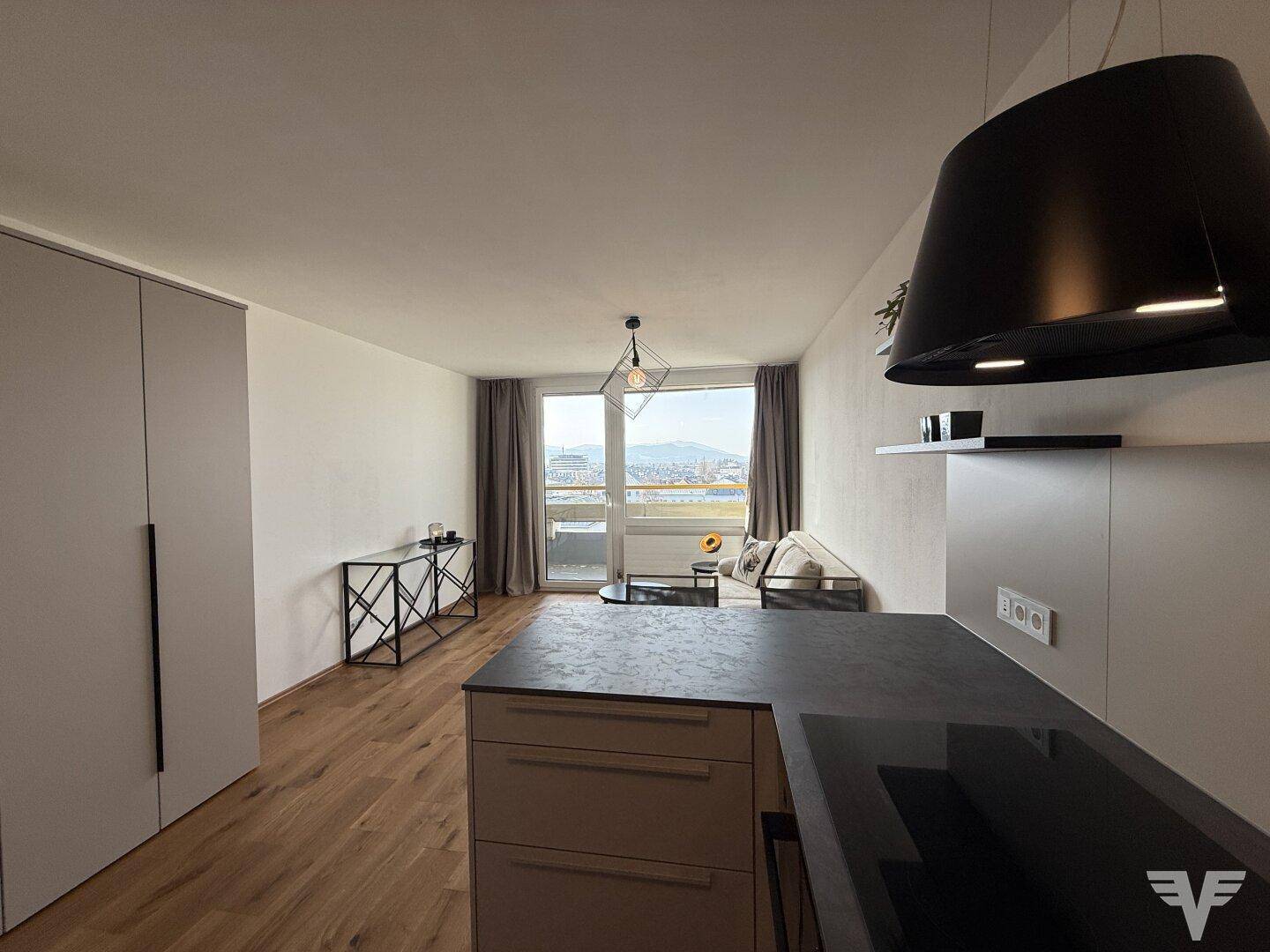 Heller Wohnbereich mit Zugang zum Balkon und Blick auf die moderne offene Küche.