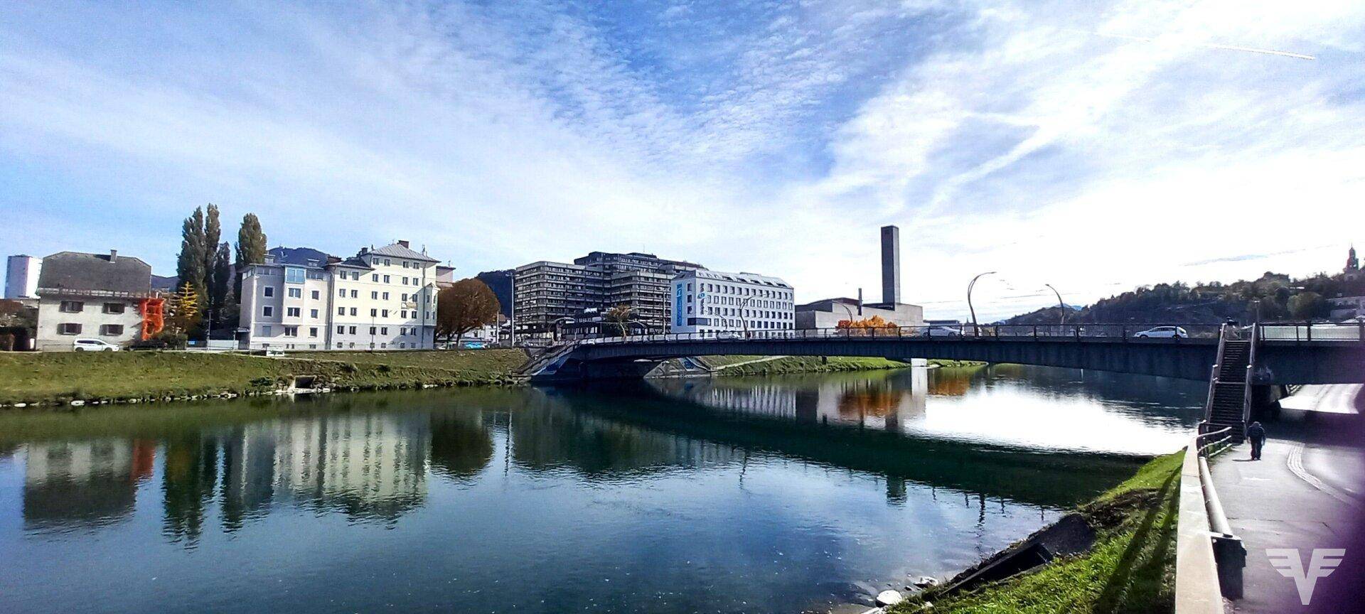 Panoramablick auf die Stadt mit Fluss, Brücke und umliegenden Gebäuden unter blauem Himmel.