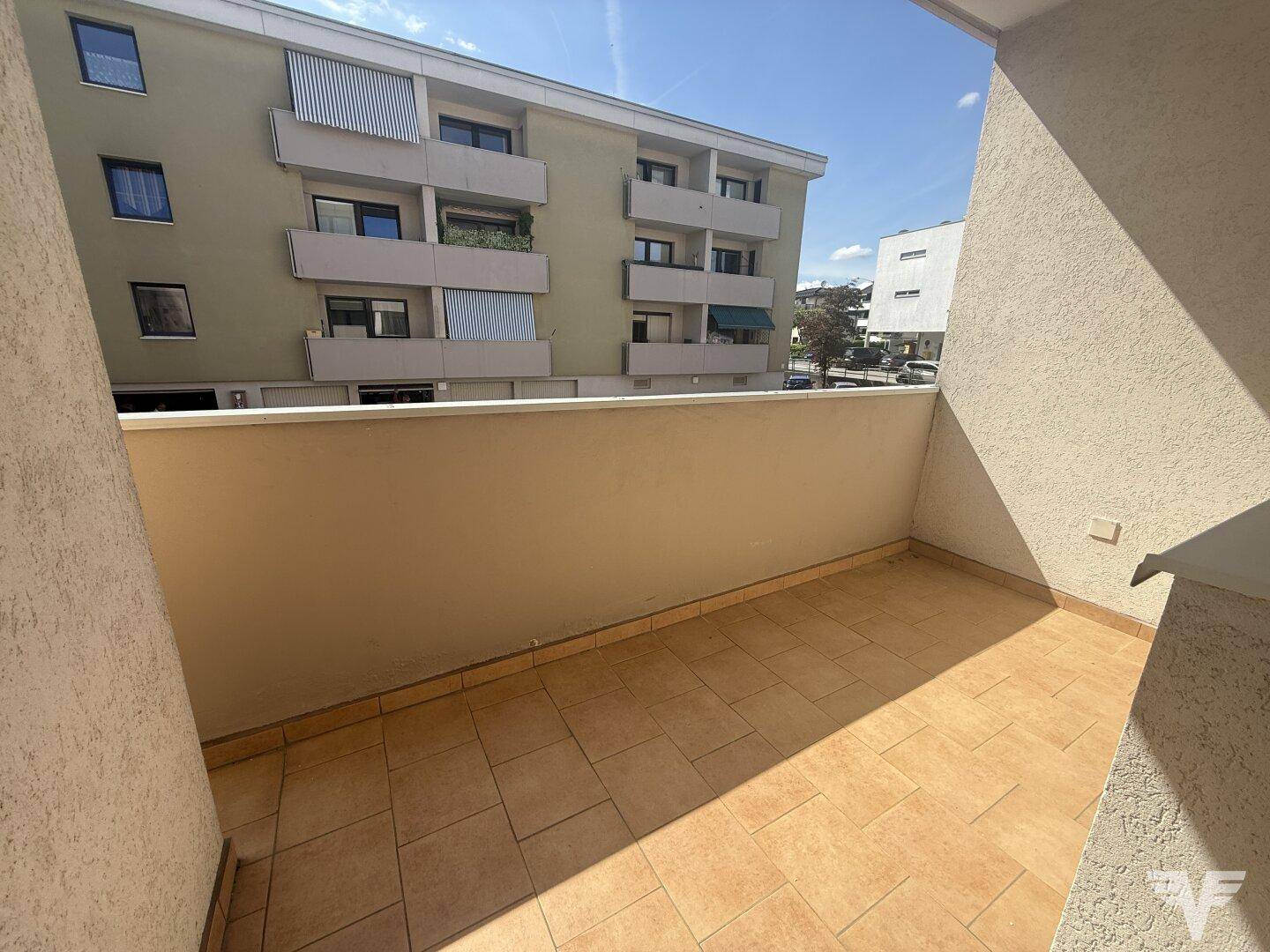 Heller Balkon mit beigefarbenen Fliesen und Blick auf die umliegenden Gebäude.
