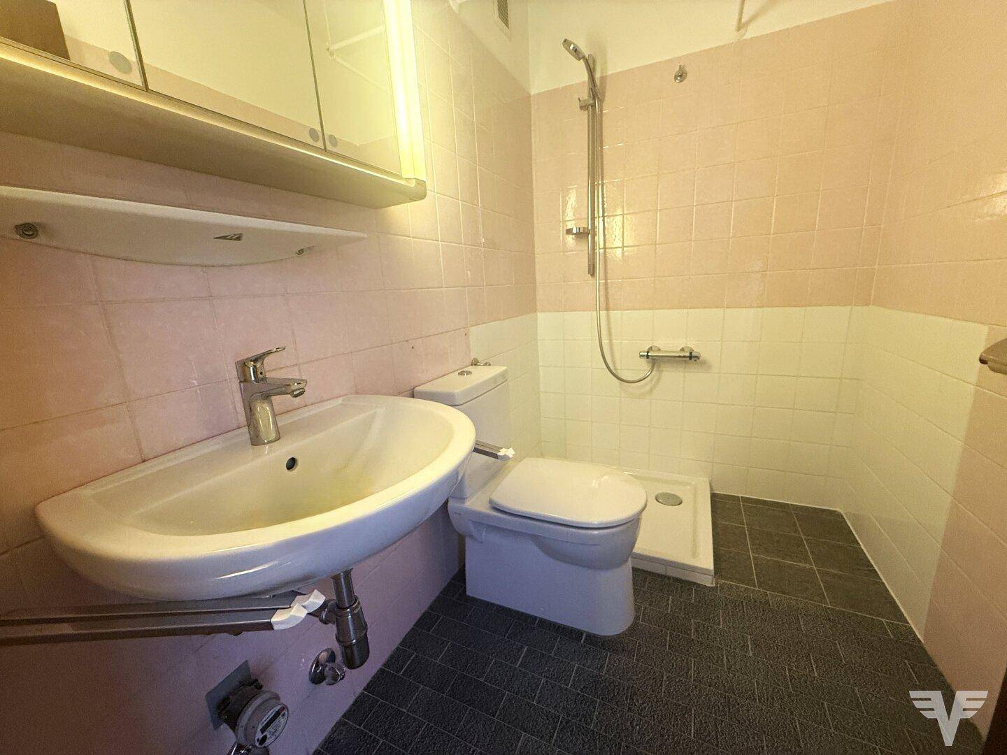 Badezimmer mit rosa Fliesen, Waschbecken, Toilette und Duschbereich.