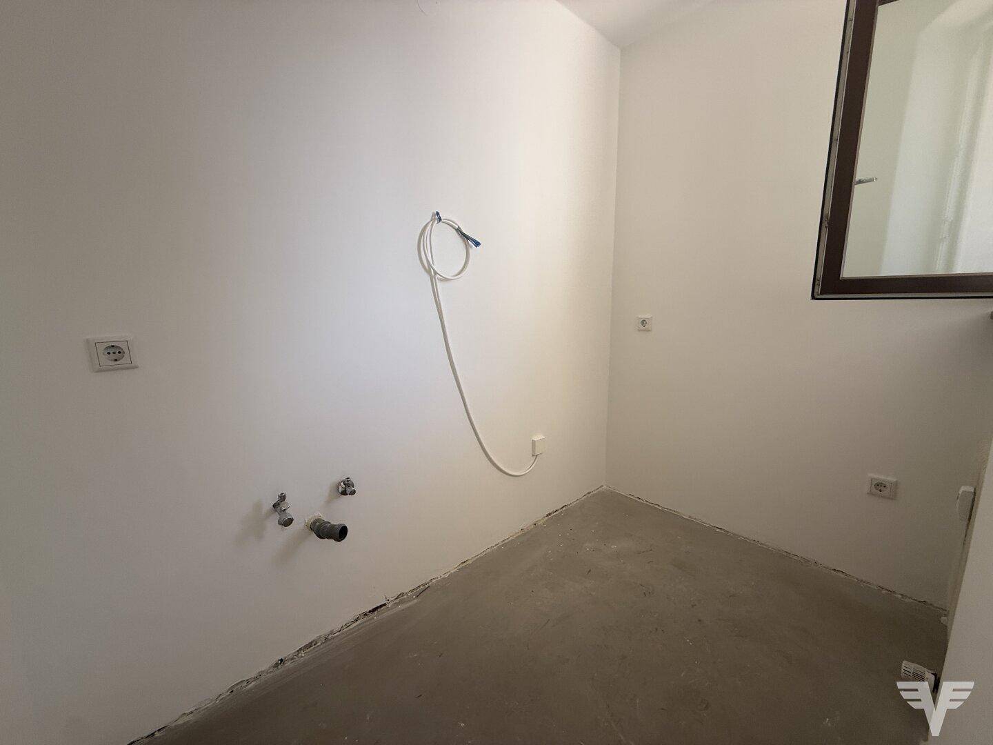 Leerer Küchenbereich mit Anschlüssen, bereit für die Installation einer Einbauküche.