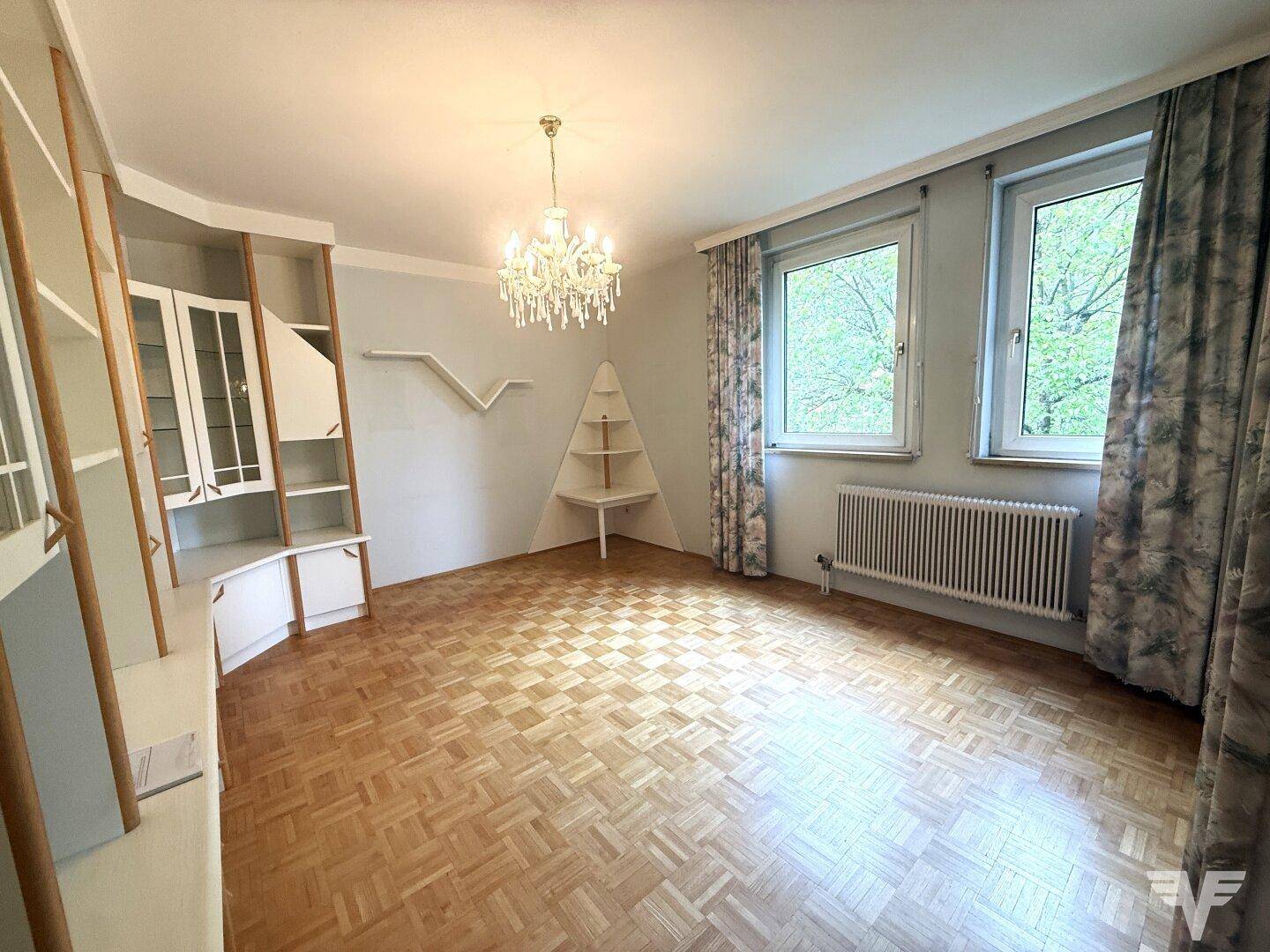Helles Wohnzimmer mit Parkettboden, Einbauschränken und einem eleganten Kronleuchter.