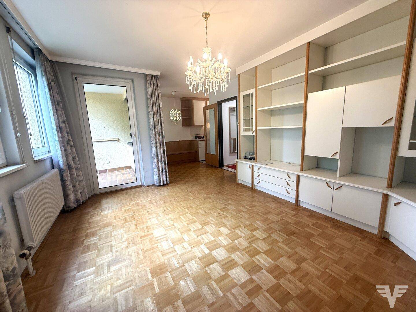Geräumiges Wohnzimmer mit Parkettboden, Einbauregalen und Zugang zu einem Balkon.