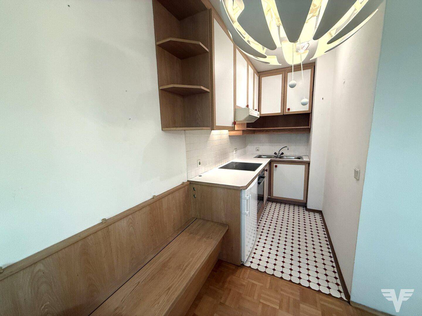 Kleine Küche mit Holzbank, weißen Oberschränken und gemustertem Fliesenboden.