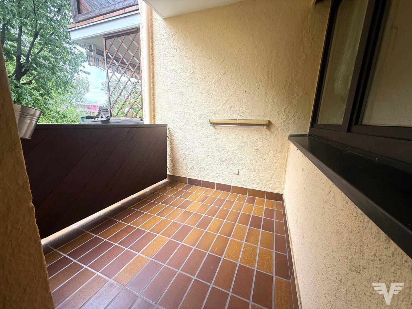 Gefliester Balkon mit braunem Sichtschutz und Blick auf Bäume und Nachbargebäude.