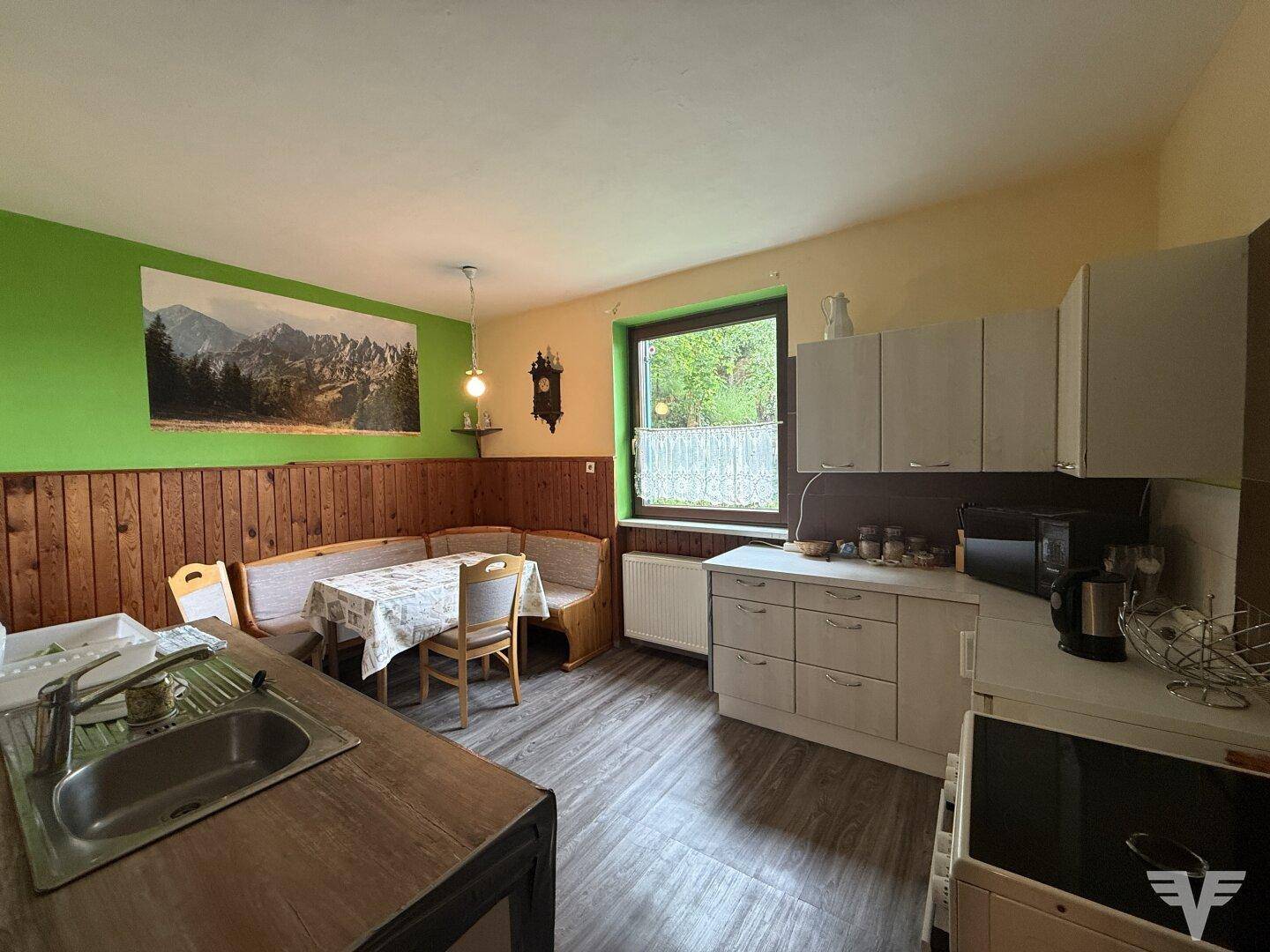 Wohnliche Küche mit Essbereich, Holzvertäfelung und Blick ins Grüne durch das Fenster, sehr einladend.
