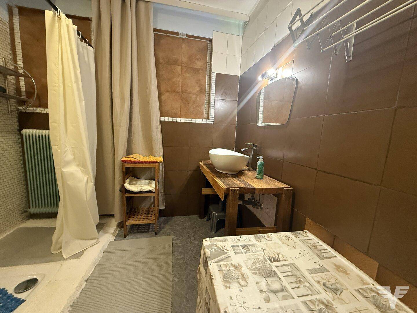 Rustikales Badezimmer mit braunen Fliesen, Duschvorhang und einfachem Waschbecken auf Holzunterschrank.