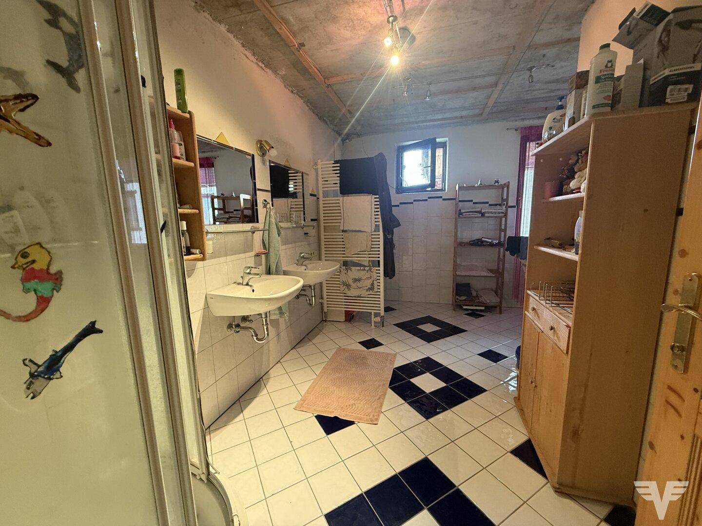 Großes Badezimmer mit schwarz-weißen Fliesen, zwei Waschbecken und Duschkabine, mit Fenster.