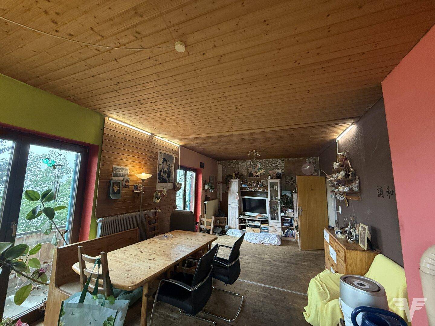 Geräumiger Wohn-Essbereich mit Holztisch, Holzdecke und Zugang zu einem Balkon, hell und offen.