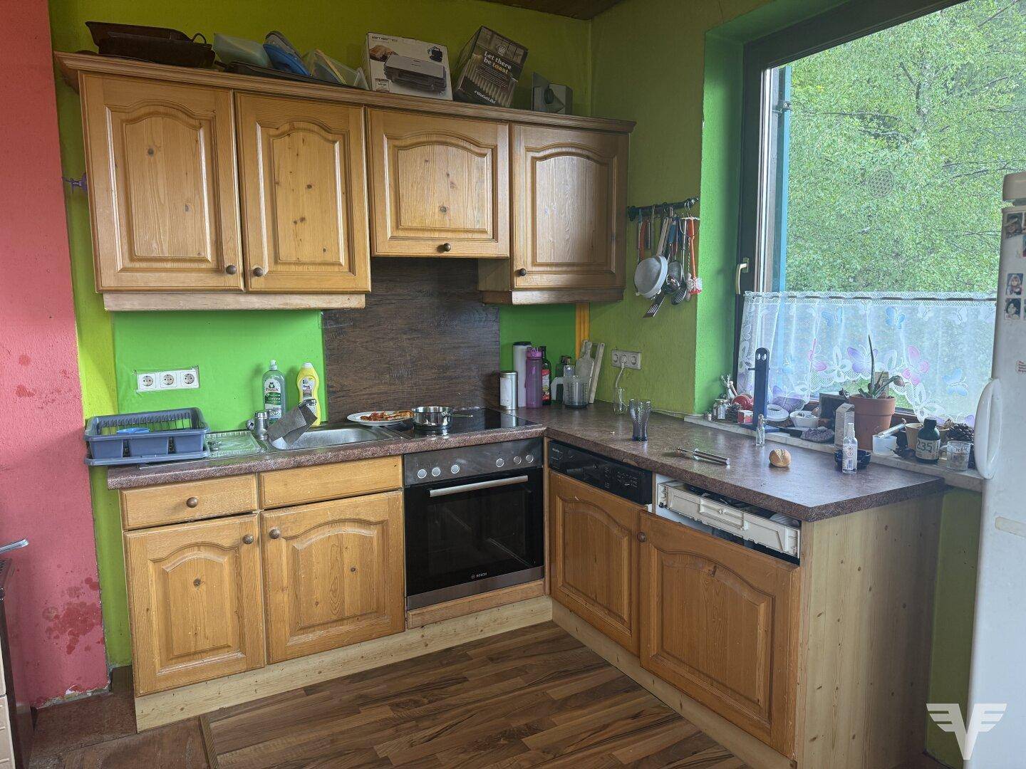 Funktionale Küche mit Holzschränken, integriertem Backofen und Blick ins Grüne, praktisch und hell.