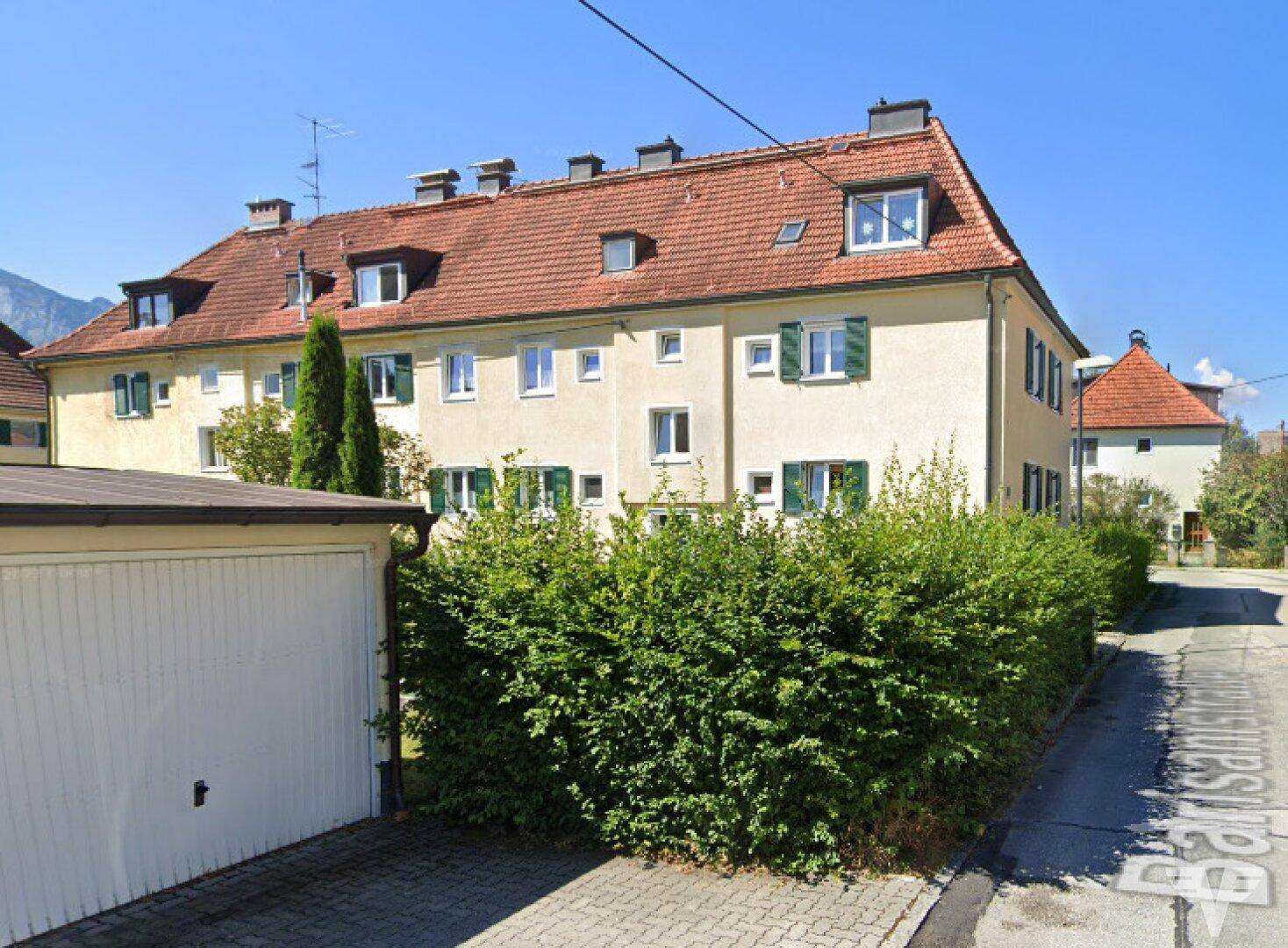 Mehrstöckiges Wohngebäude mit rotem Ziegeldach und grünen Fensterläden in einer ruhigen Wohngegend.