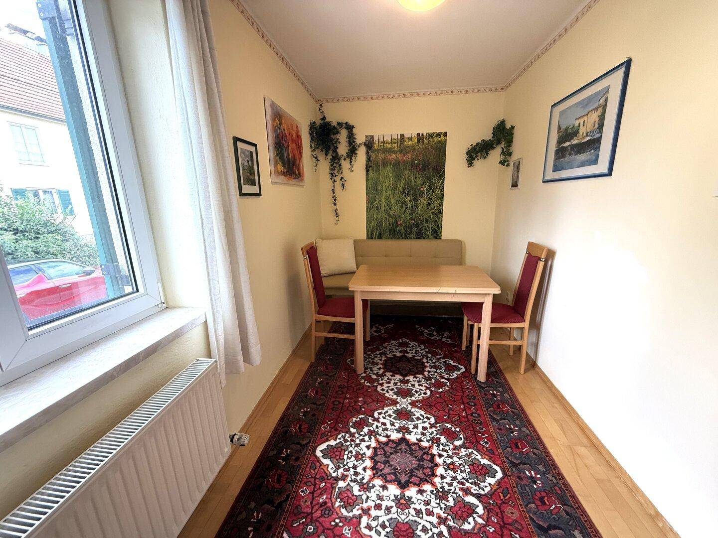 Gemütlicher Essbereich mit Holztisch, roten Stühlen und einem großen Fenster für viel Tageslicht.