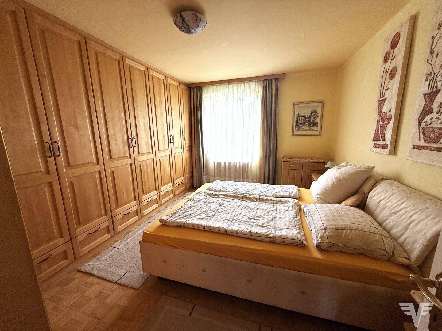 Helles Schlafzimmer mit großem Holzschrank, Doppelbett und Parkettboden.