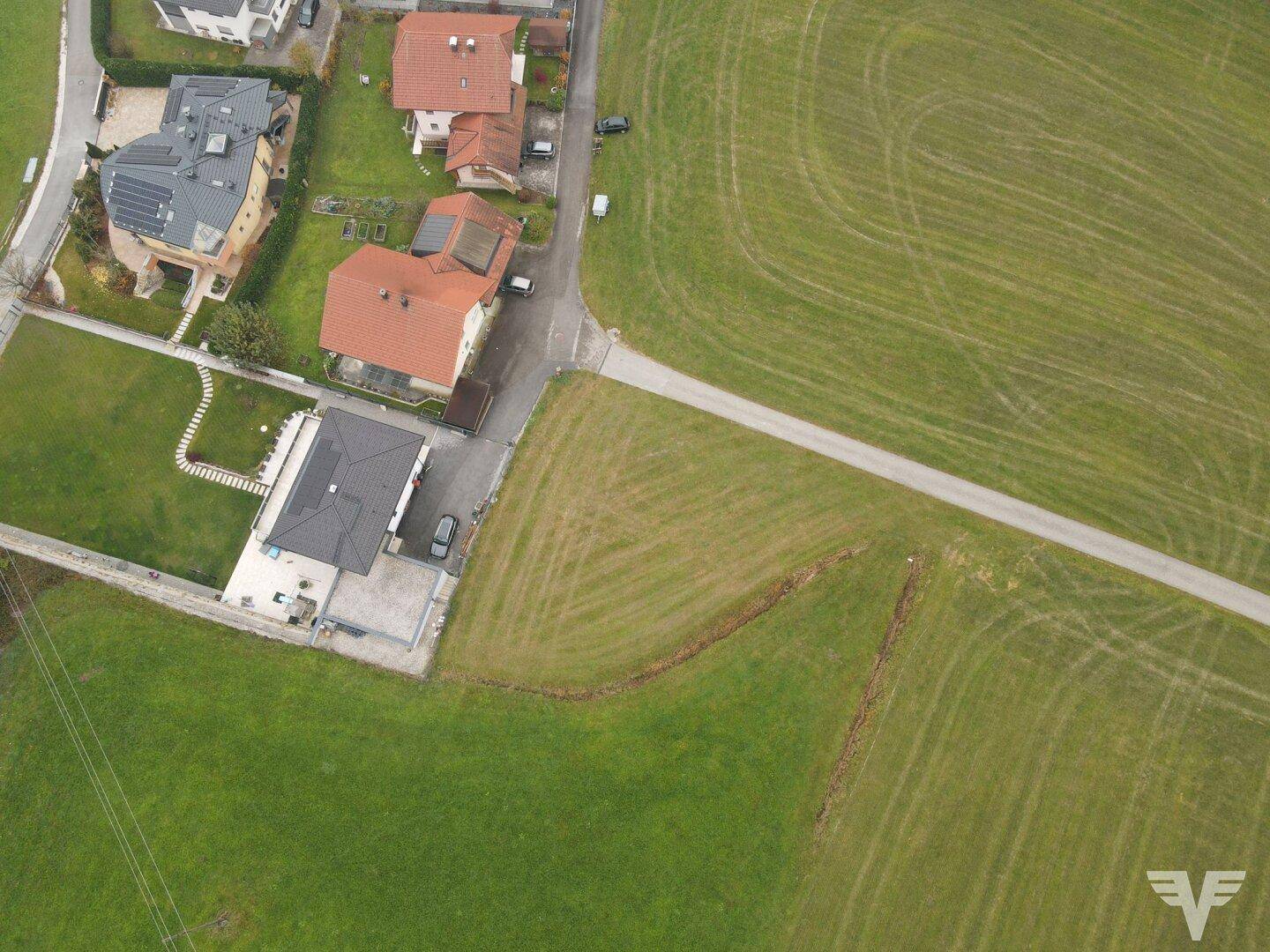 Nähere Luftaufnahme von Wohnhäusern und weiten grünen Feldern, die eine ländliche Straße zeigen.