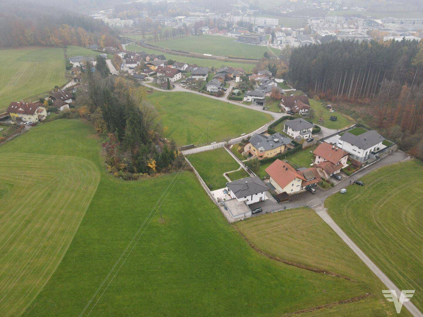 Weitläufige Luftansicht eines Wohngebiets, umgeben von Natur und Wald, mit einem Baugrundstück.