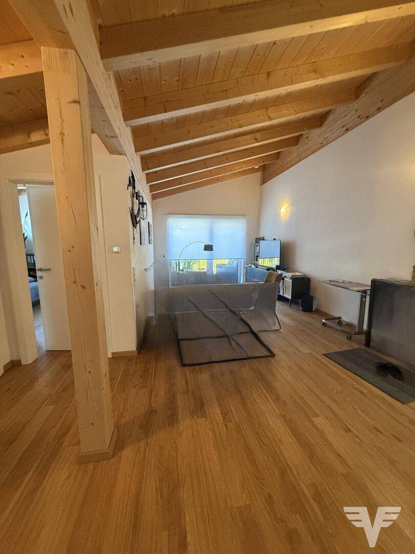 Heller Wohnbereich mit sichtbaren Holzbalken, Holzboden und einem modernen Kamin, der eine gemütliche Atmosphäre schafft.