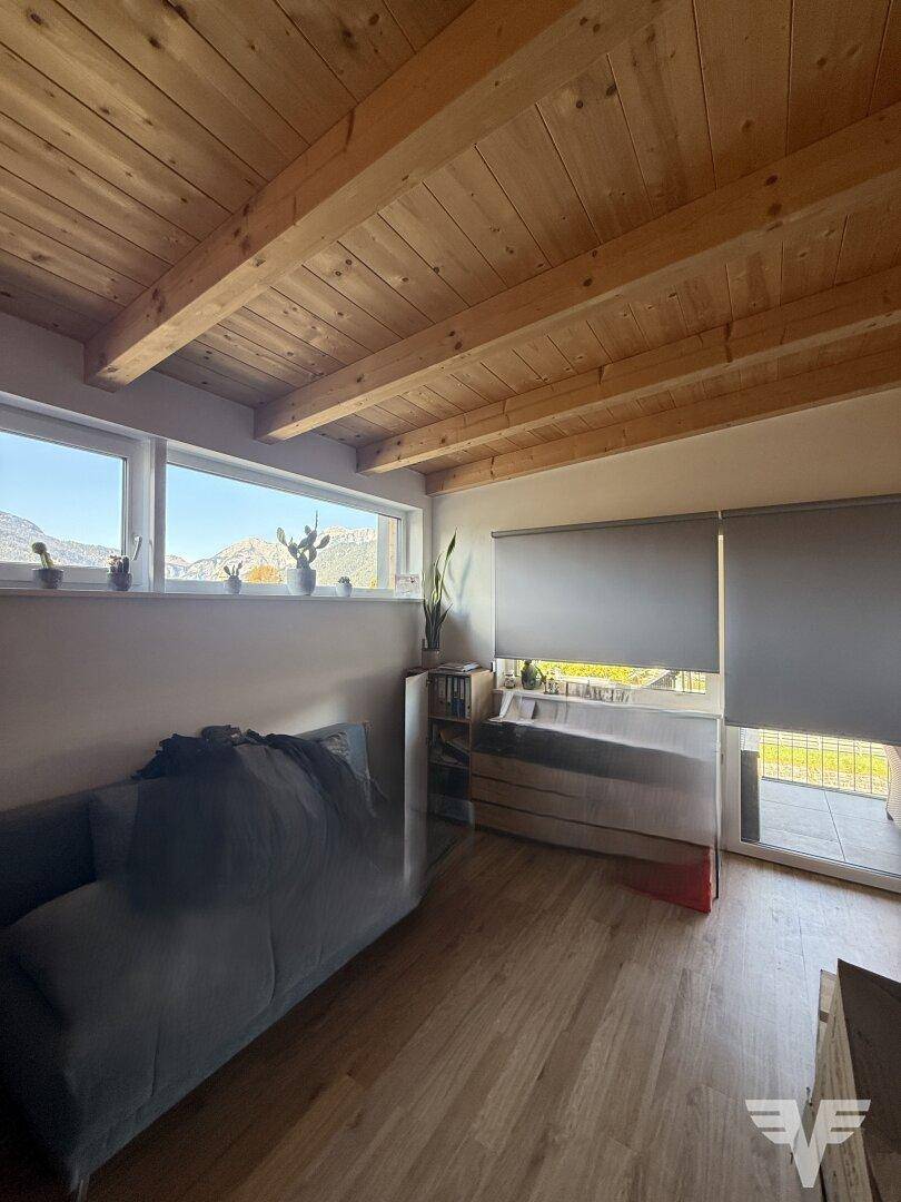Gemütliches Wohnzimmer mit Holzbalkendecke, Holzboden und großen Fenstern mit Blick auf die umliegende Landschaft.