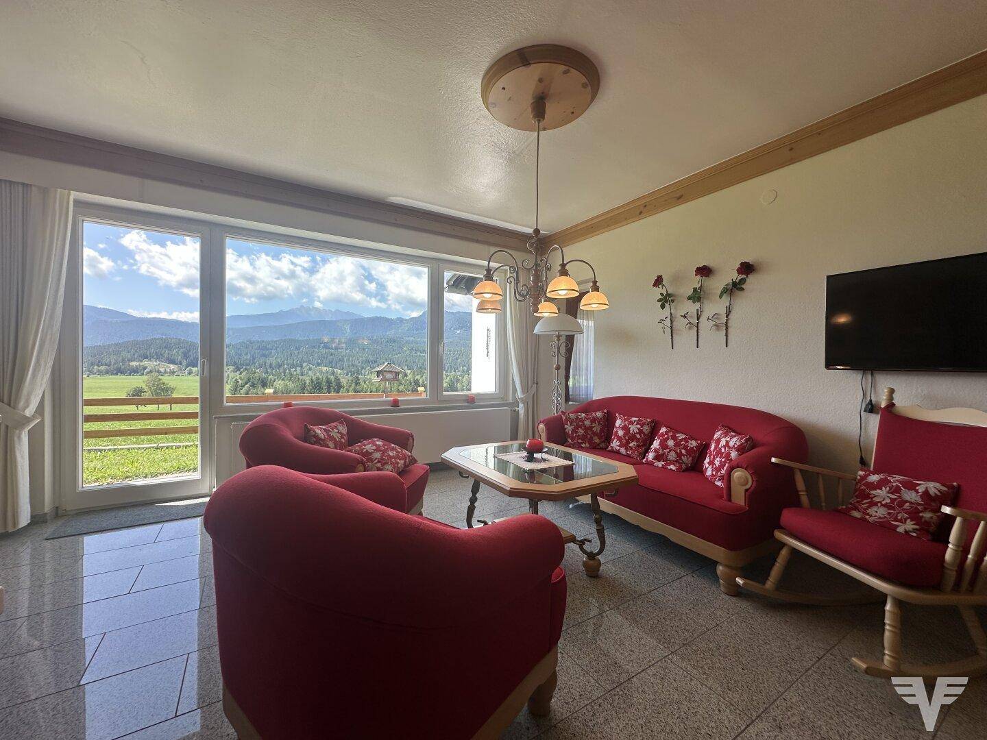 Gemütliches Wohnzimmer mit roten Möbeln, Fliesenboden und weitem Bergblick durch große Fenster.