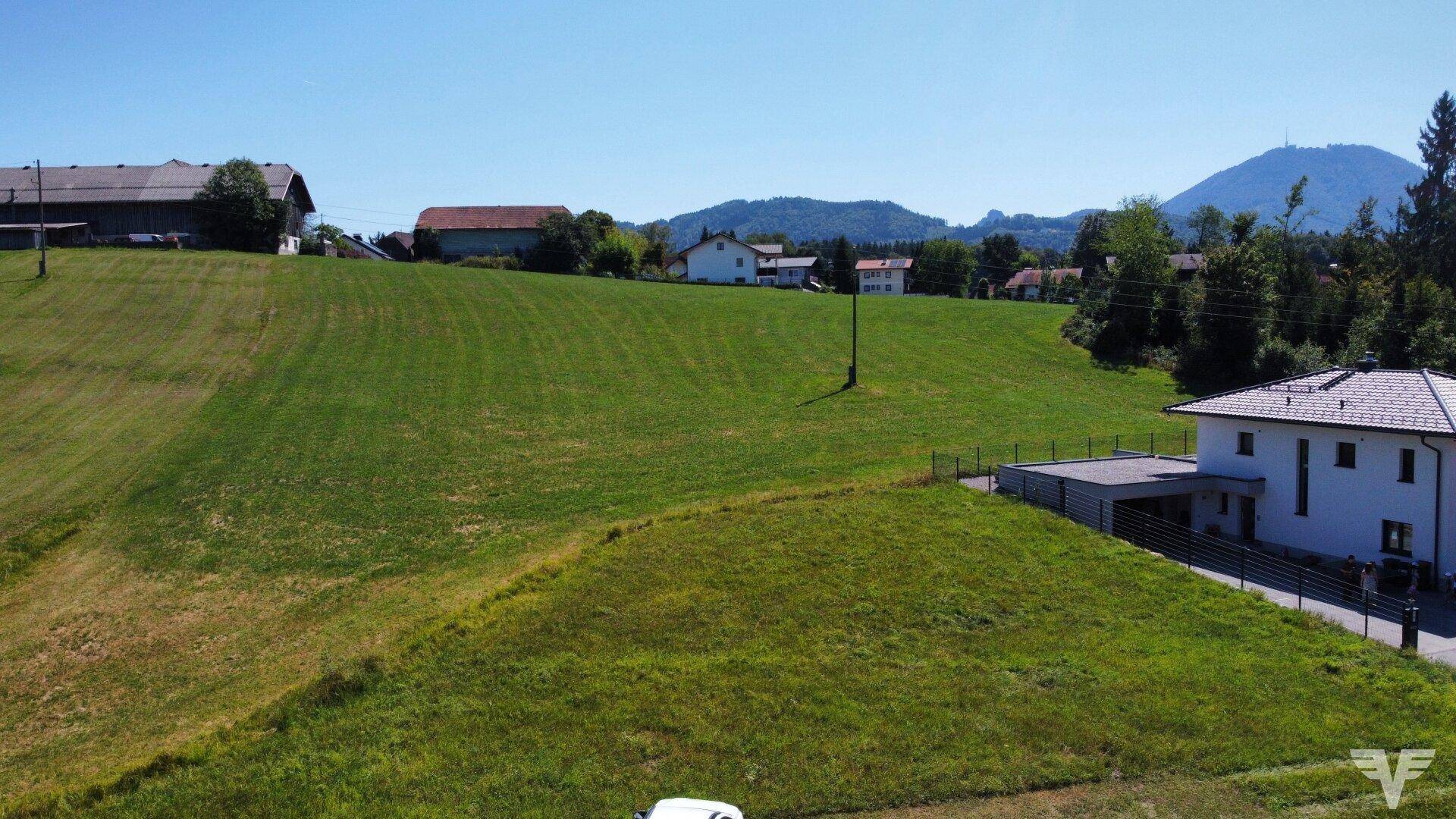 Weitläufige Luftaufnahme eines modernen Hauses neben grünen Feldern mit Bergblick in der Ferne.