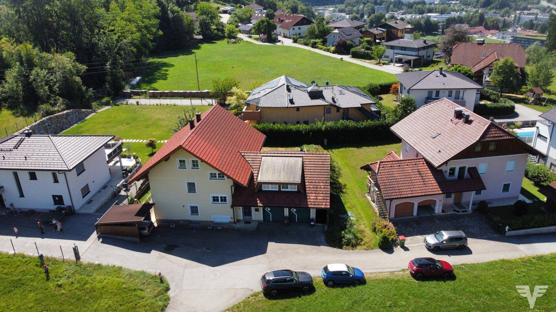 Panoramablick auf eine Wohnsiedlung mit verschiedenen Häusern und grünen Hügeln im Hintergrund.