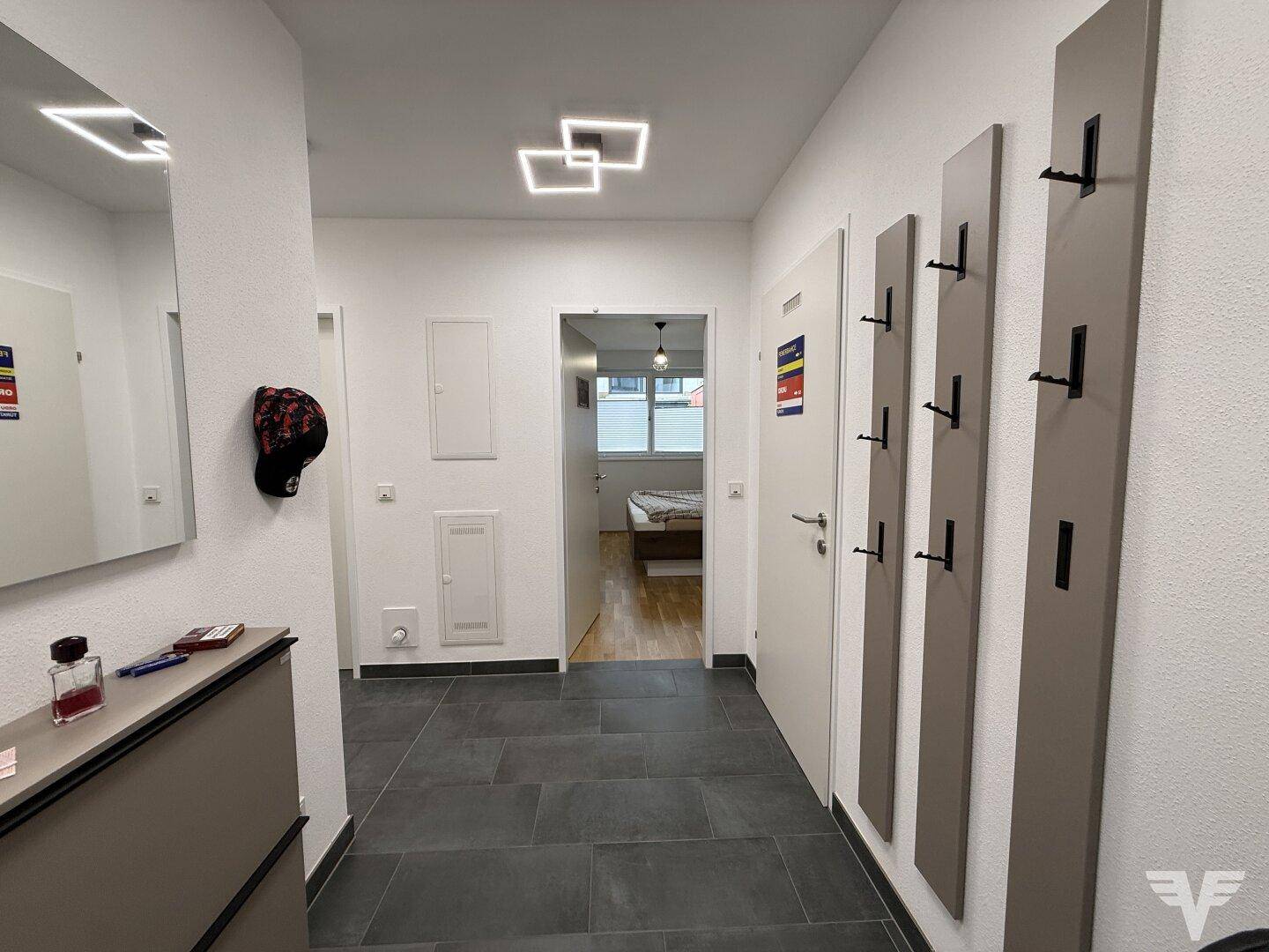 Moderner Eingangsbereich mit dunklen Fliesen, Spiegel, Schuhschrank und Garderobe.