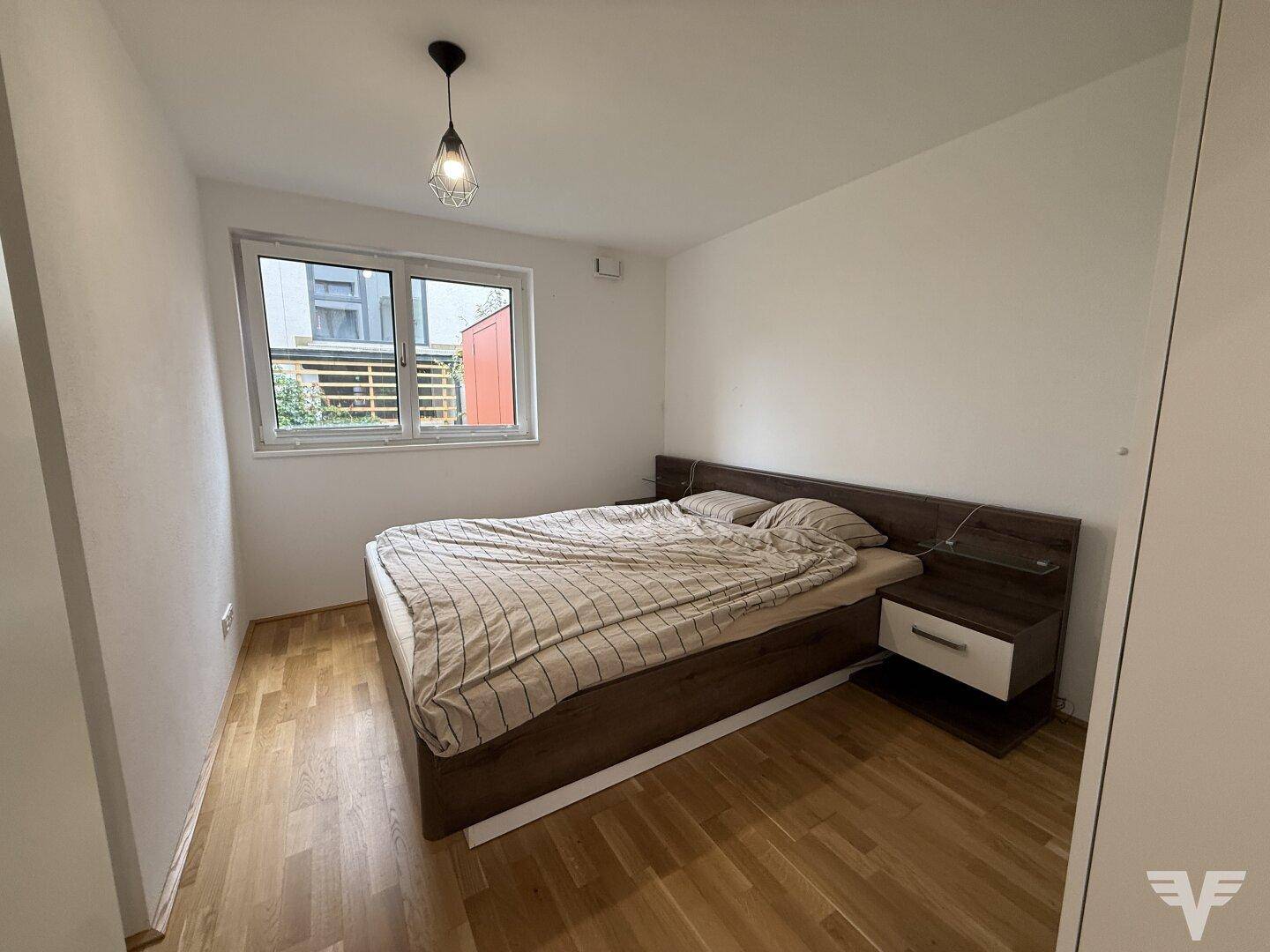 Gemütliches Schlafzimmer mit Holzboden und großem Fenster für viel Tageslicht.