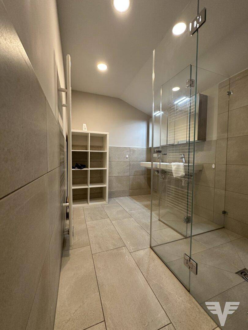 Modernes Badezimmer mit begehbarer Dusche, grauen Fliesen und Handtuchheizkörper.