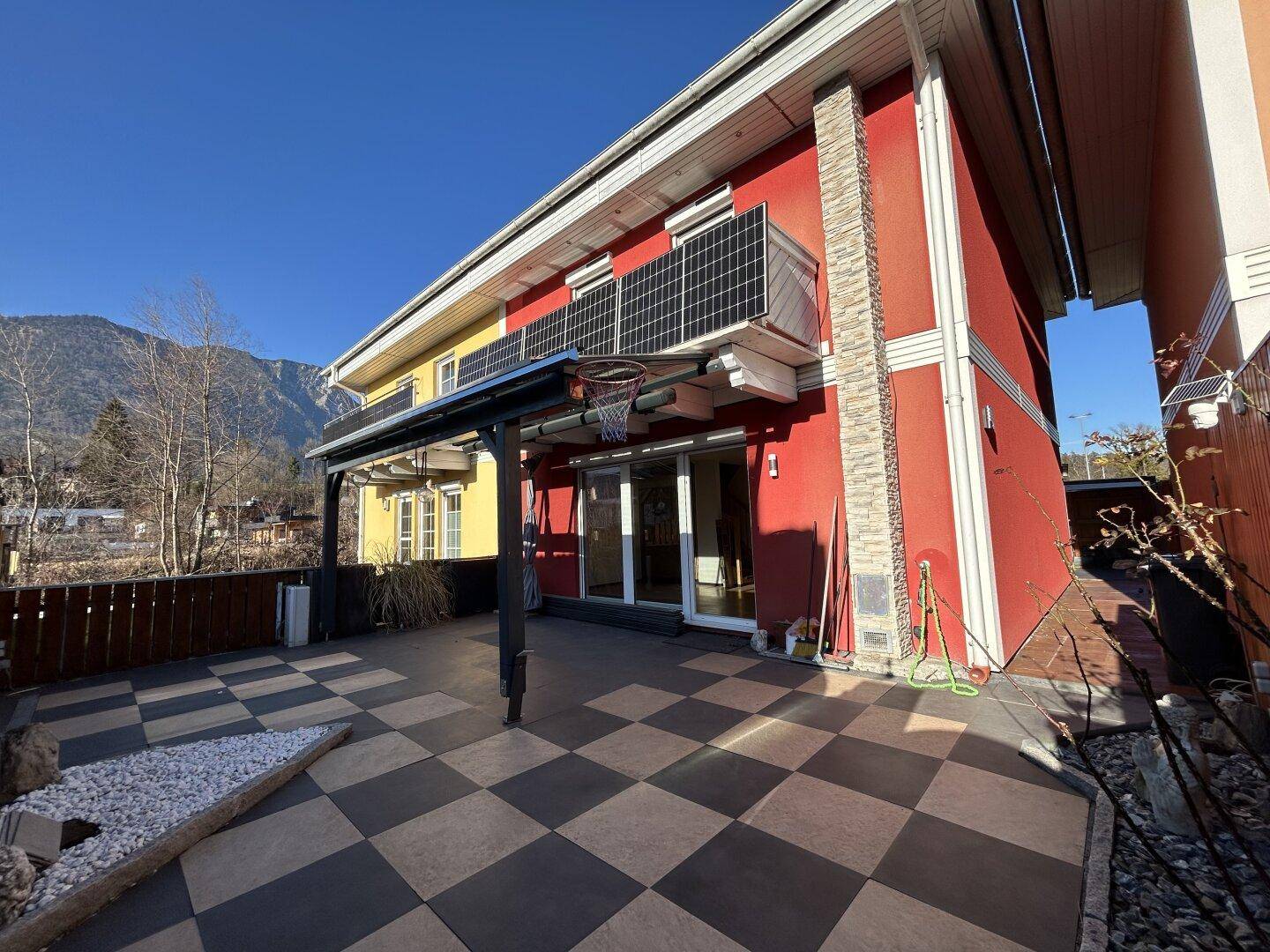 Große, geflieste Terrasse mit Schachbrettmuster, überdachter Pergola und Bergblick.