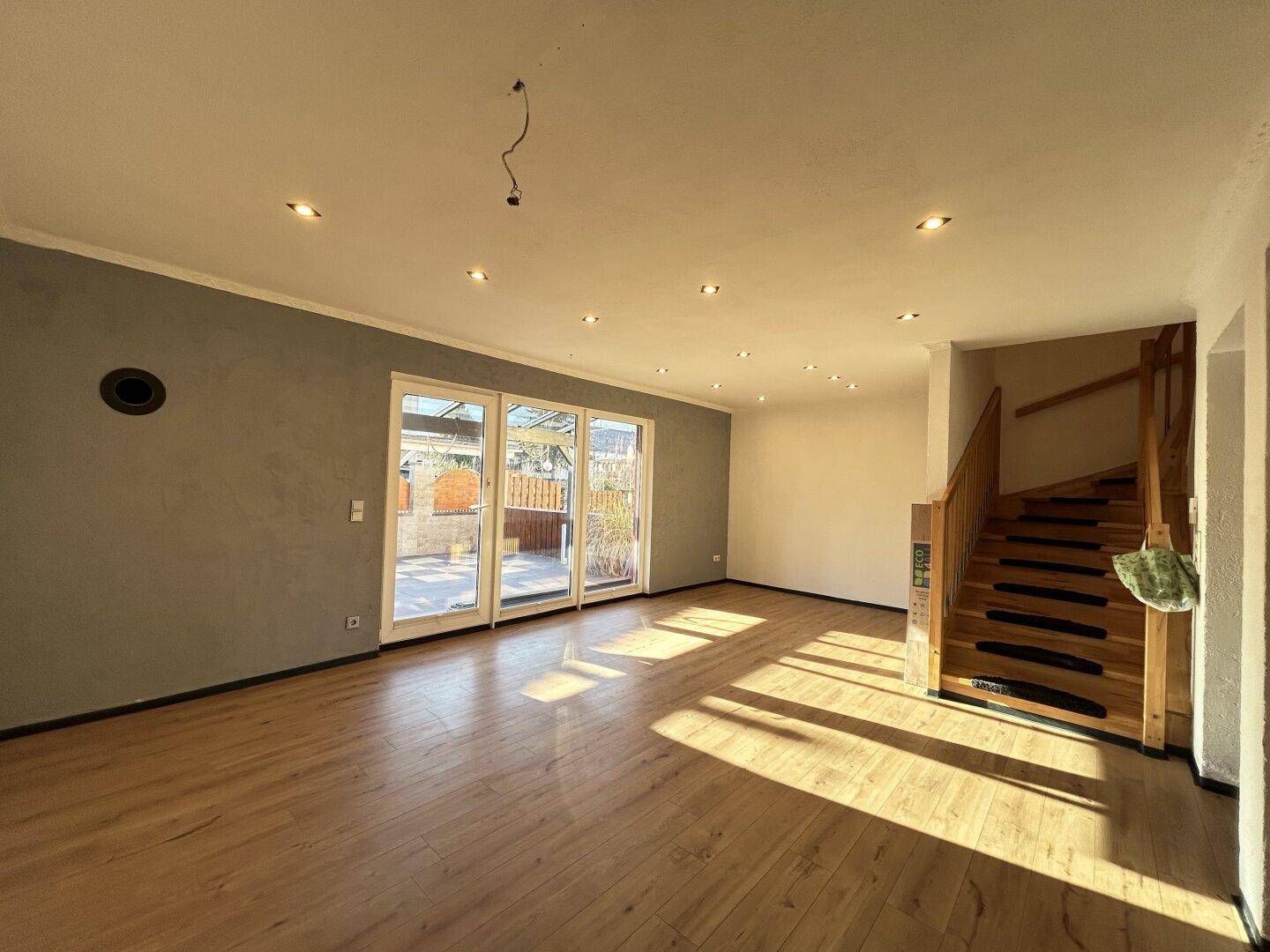 Geräumiger Wohnbereich mit Laminatboden, Holztreppe und direktem Zugang zur sonnigen Außenterrasse.