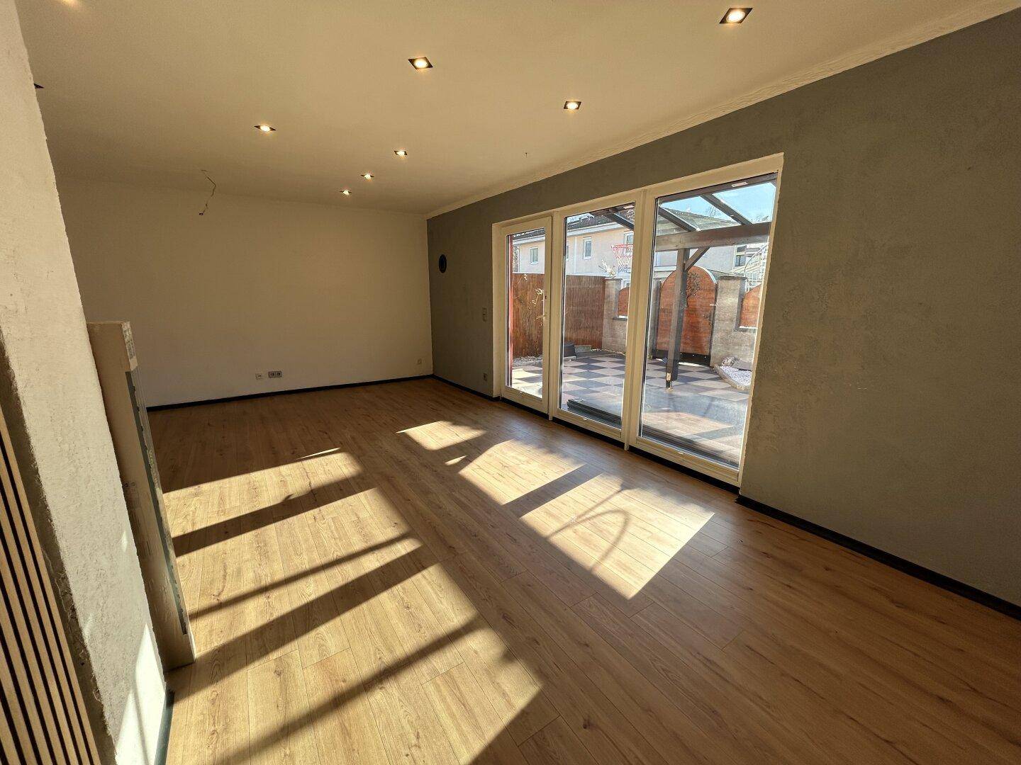 Helles Wohnzimmer mit Laminatboden, Einbaustrahlern und Zugang zu einer gefliesten Terrasse.
