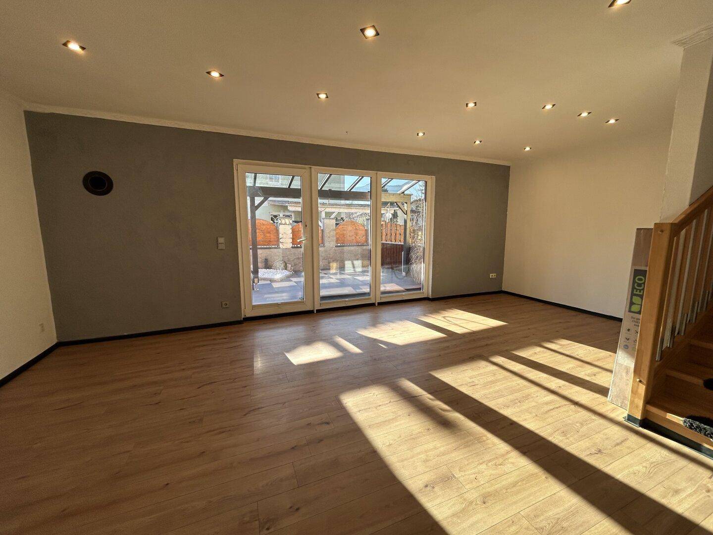 Lichtdurchfluteter Wohnbereich mit Laminatboden, Holztreppe und großzügigem Terrassenzugang.