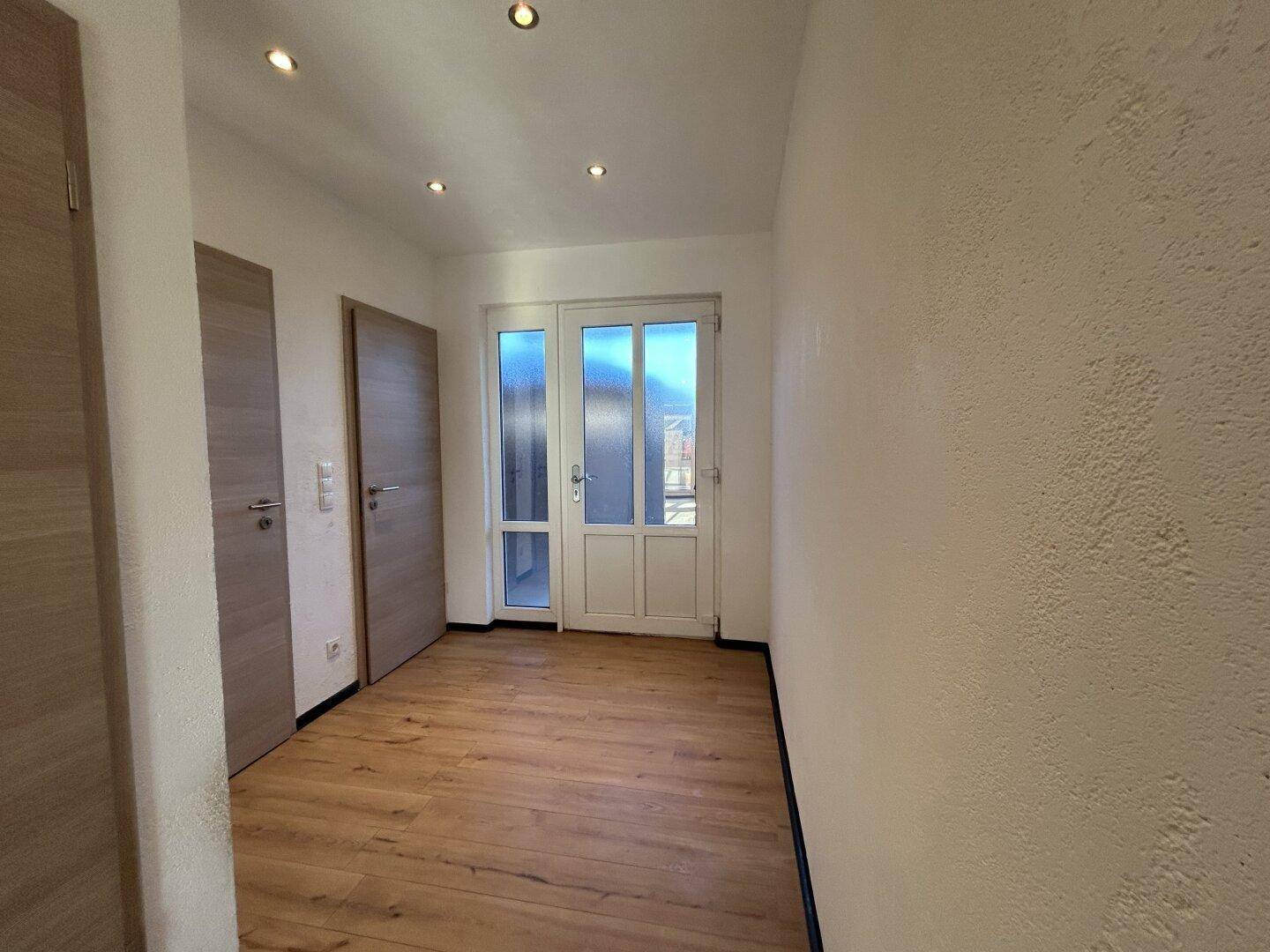 Heller Flur mit Laminatboden, Einbaustrahlern und einer Tür, die zu einem Außenbereich führt.
