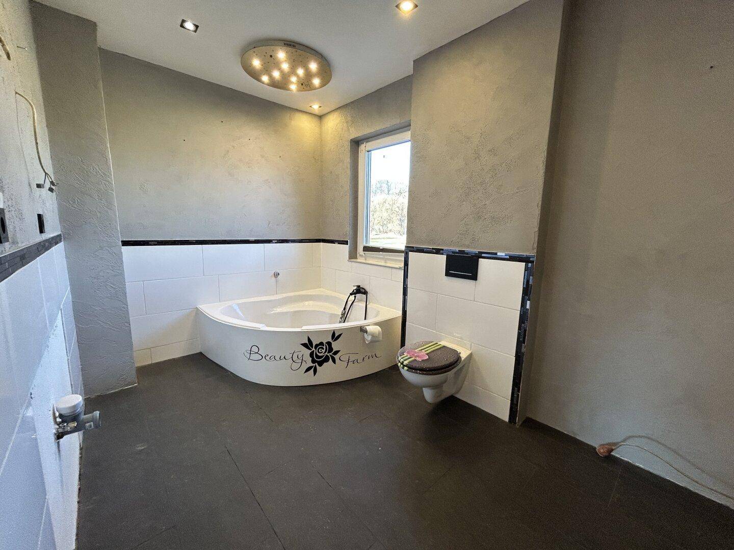 Badezimmer in Renovierung mit Eckbadewanne, wandhängendem WC und Fenster für Tageslicht.