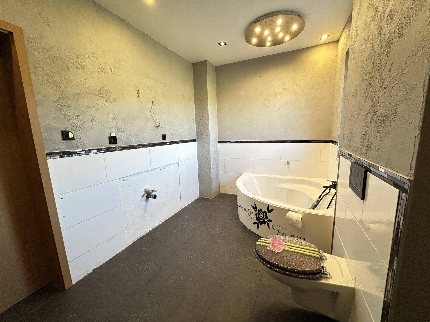 Renovierungsbedürftiges Badezimmer mit Eckbadewanne, wandhängendem WC und vorbereitetem Waschtischbereich.