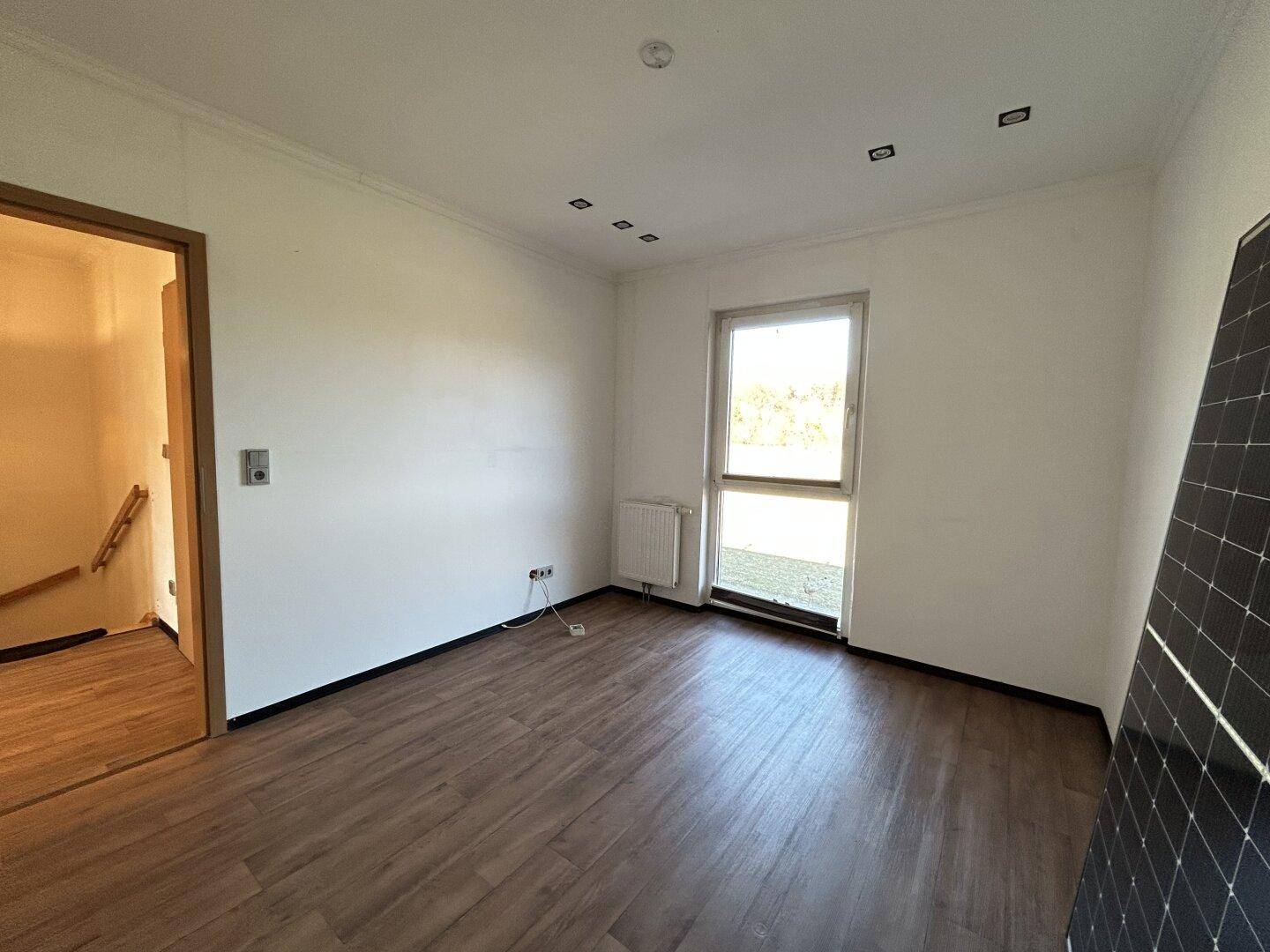 Helles Zimmer mit Laminatboden, Fenster und Heizkörper, bereit für die individuelle Gestaltung.