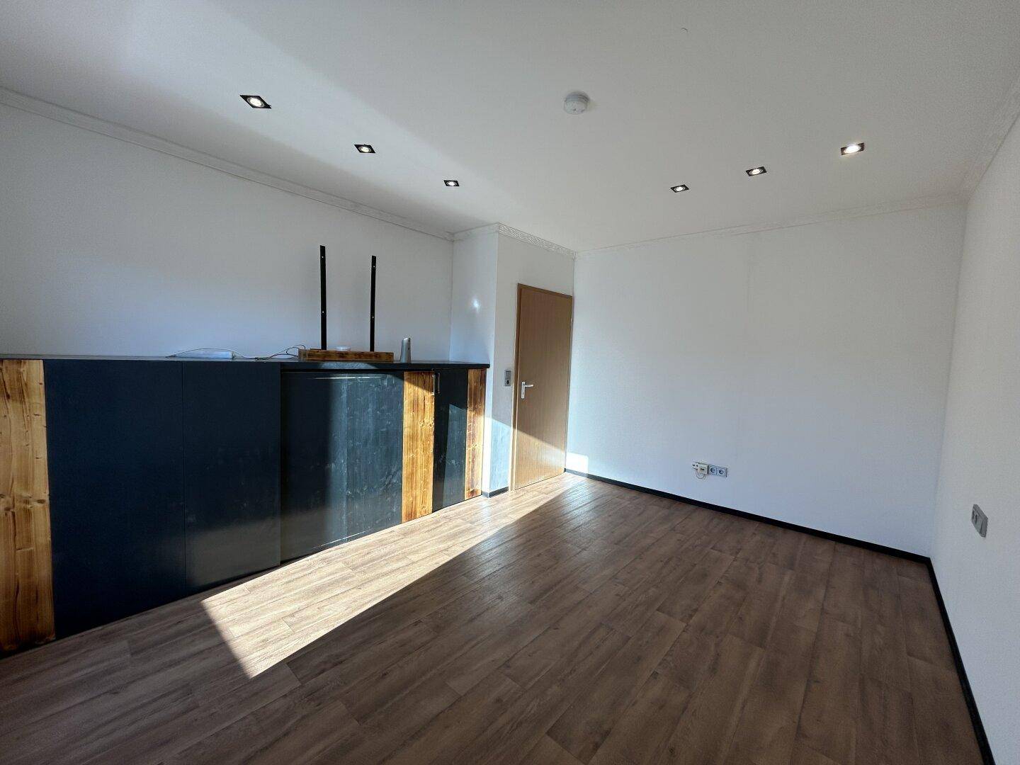 Leerer Raum mit Laminatboden, Einbaustrahlern und einer Theke mit Holzverkleidung.