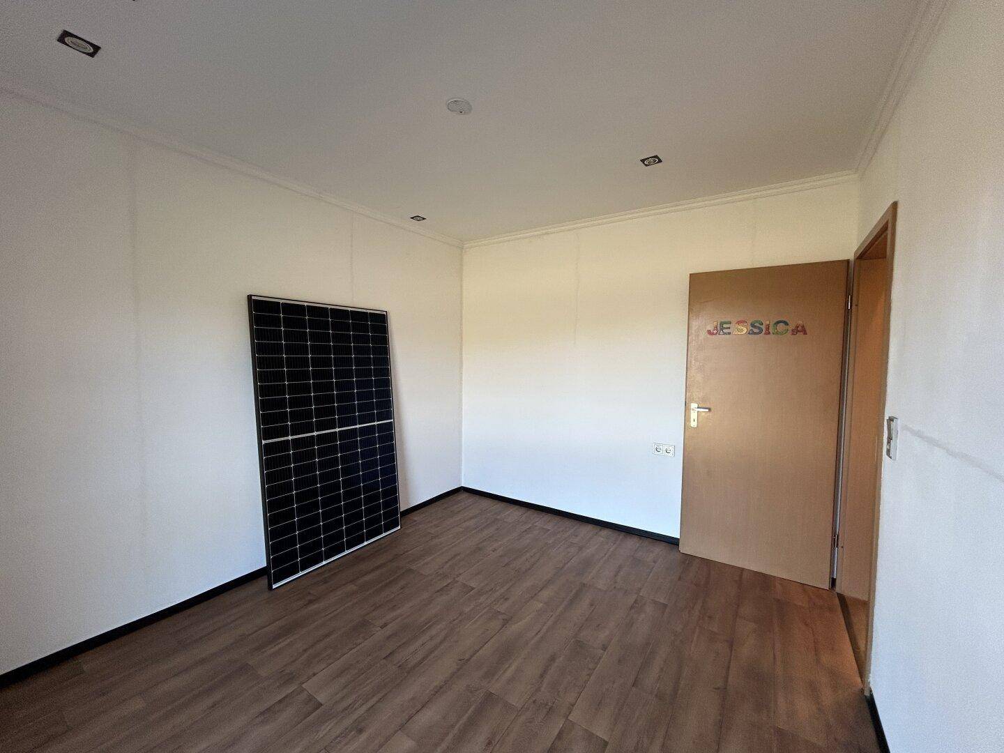 Leeres Zimmer mit Laminatboden, Einbaustrahlern und einer Tür, die zu einem weiteren Raum führt.