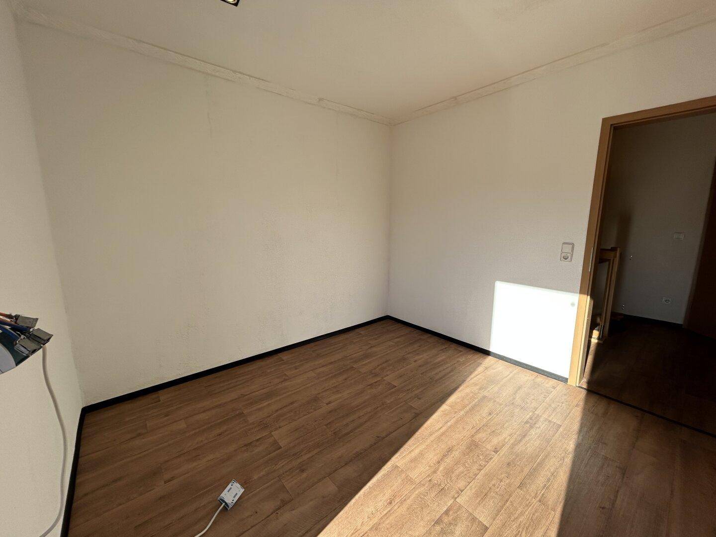 Helles Zimmer mit Laminatboden, Heizkörper und viel natürlichem Licht.