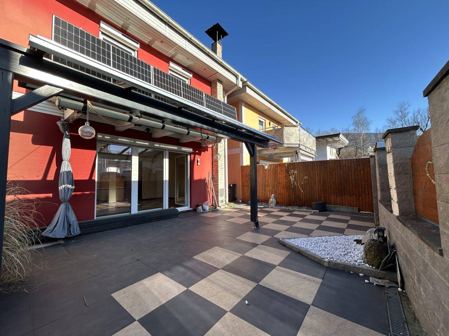 Hausfassade mit rotem Anstrich, Solarpaneelen und einer großen, überdachten Terrasse.